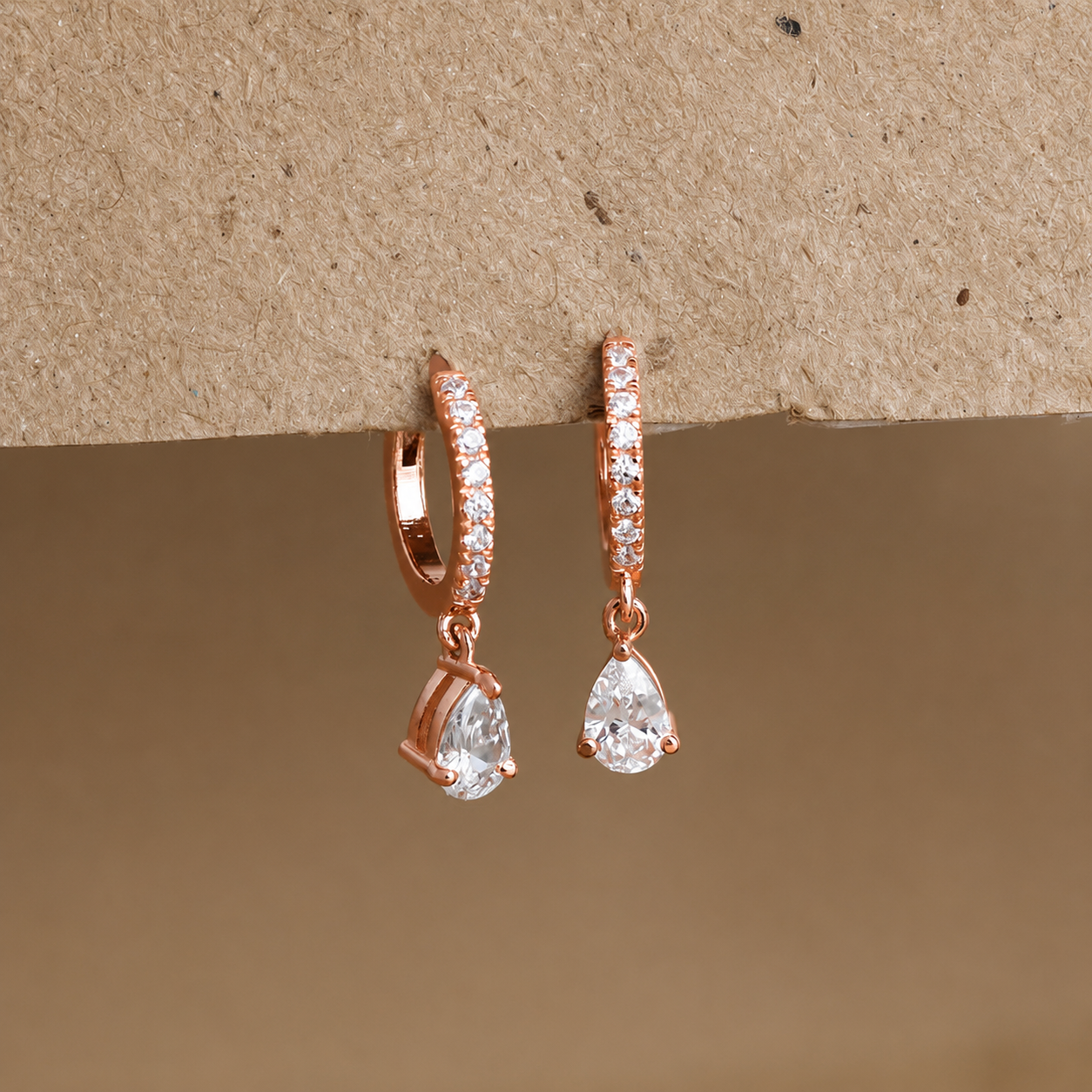 Rose gold hoop earrings with teardrop-shaped gemstones on a beige background